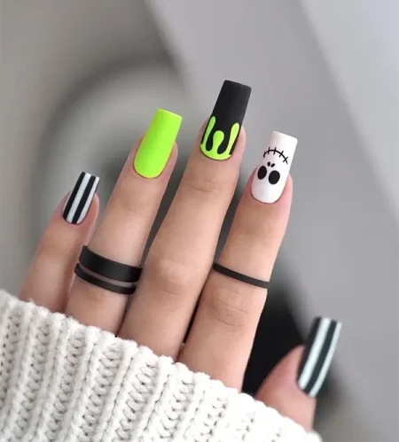 Halloween nails with black-and-white stripes, neon green accents, slime, and a ghost face design.